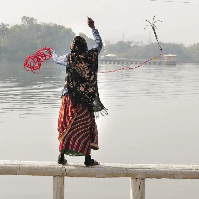 A woman and a child are standing on a railing in front of a lake and are fishing.