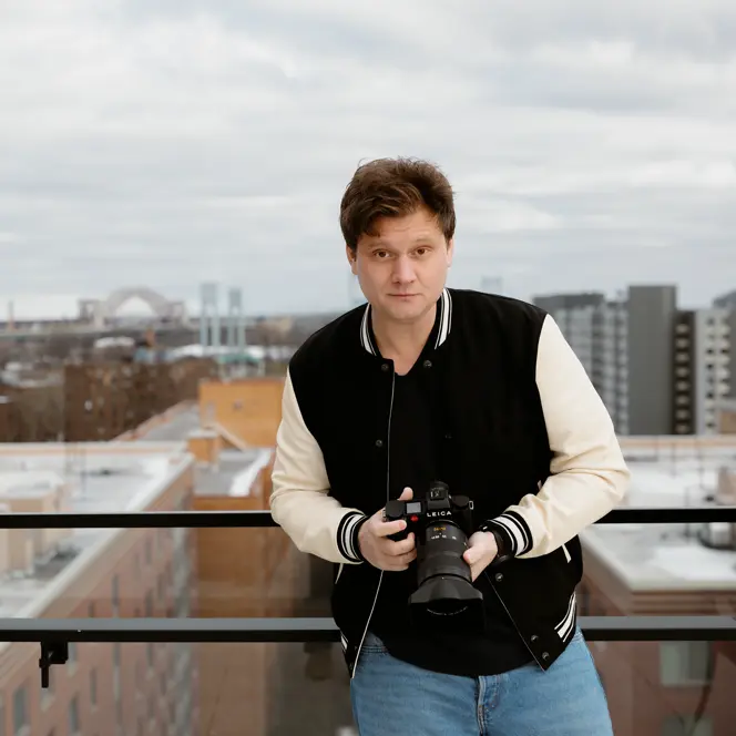 Person holding a camera, in the background are skyscrapers and a bridge on a cloudy day.