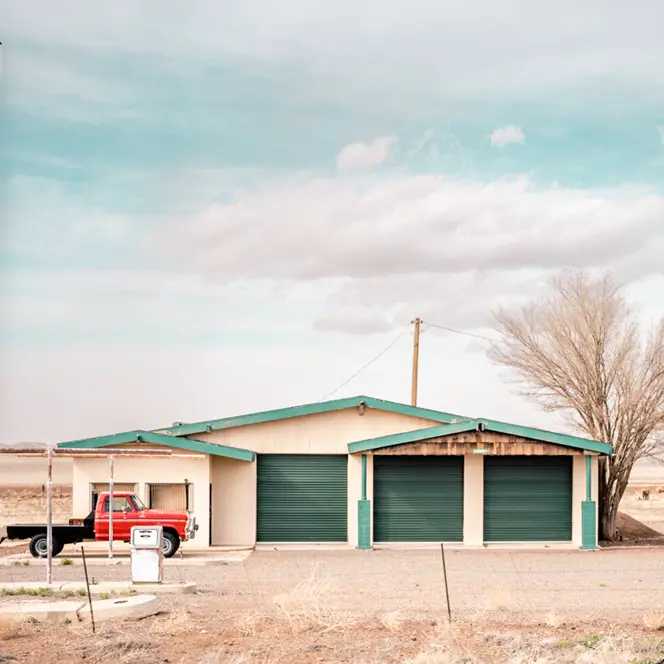 An abandoned gas station in an arid landscape with an old red truck and a caravan.