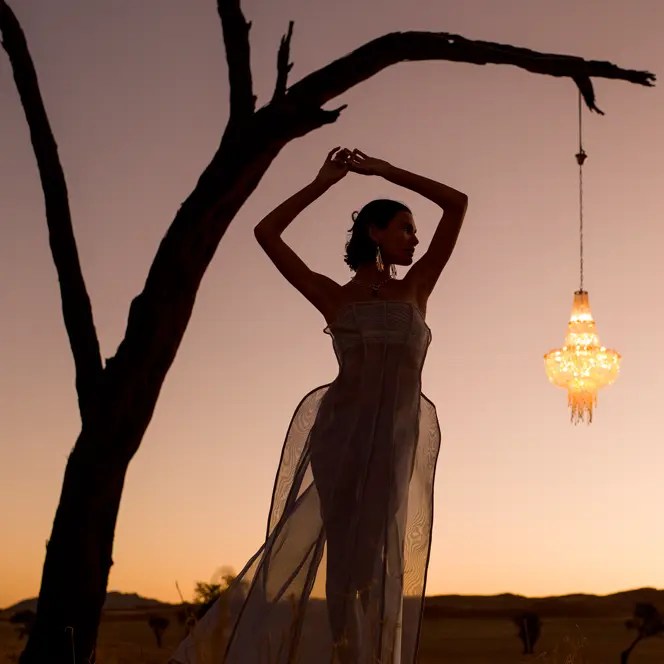 Woman posing under a tree at sunset next to a hanging lantern.