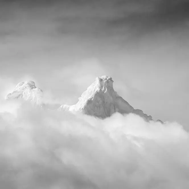 Two snow-covered mountain peaks protrude through a blanket of cloud.