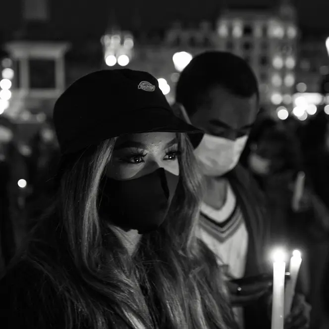 Close-up of a woman and man wearing masks and holding candles in a city at night.