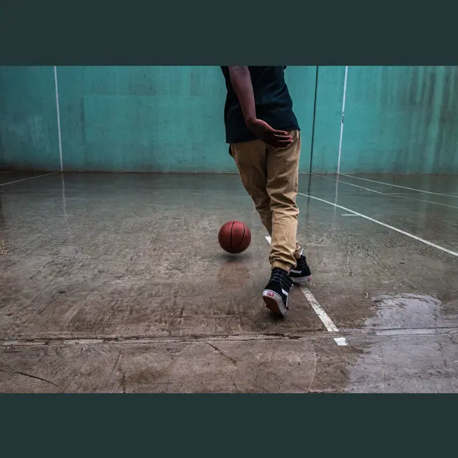 Person playing basketball on a wet court with a turquoise wall in the background.