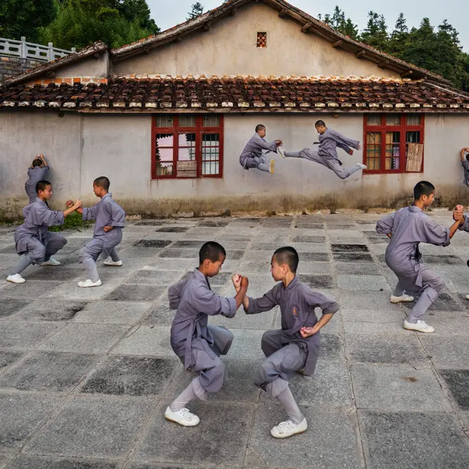 Shaolin monks practise martial arts in the courtyard in front of a traditional building