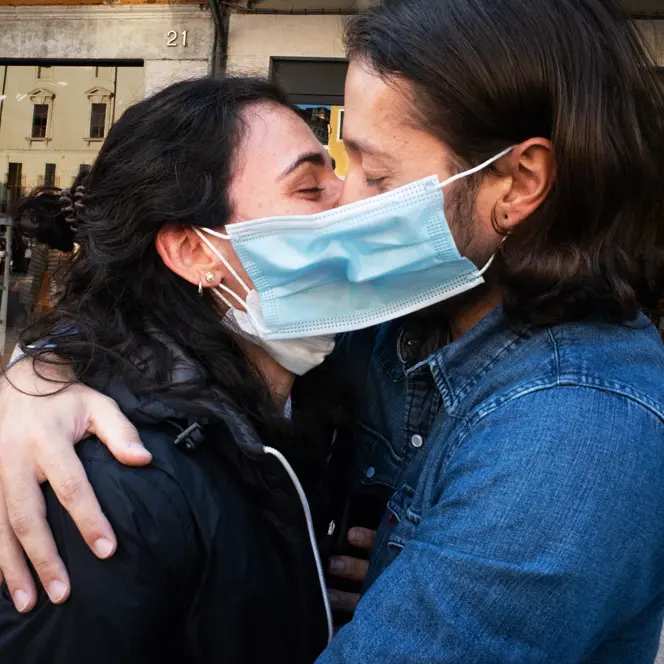 A couple wearing face masks hug and kiss in a street