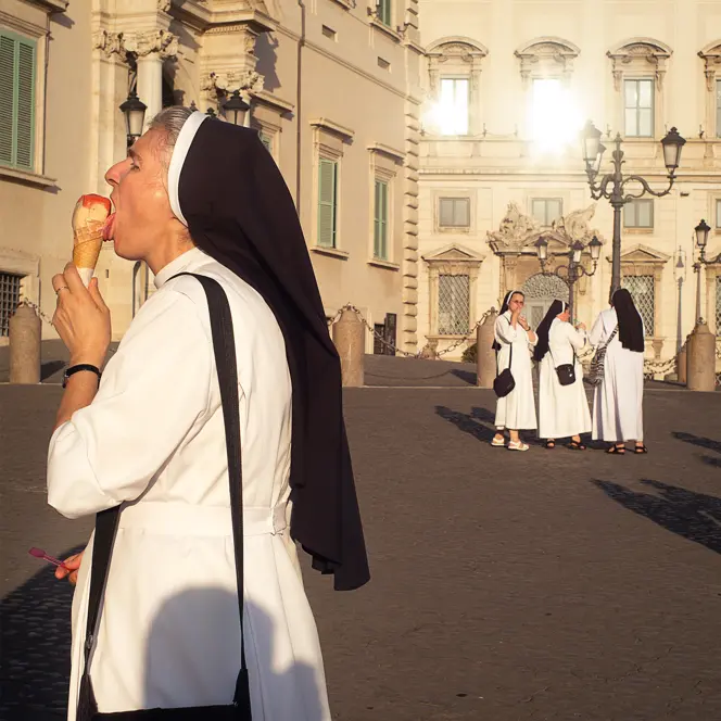 A nun eats an ice cream while several nuns talk in the background.