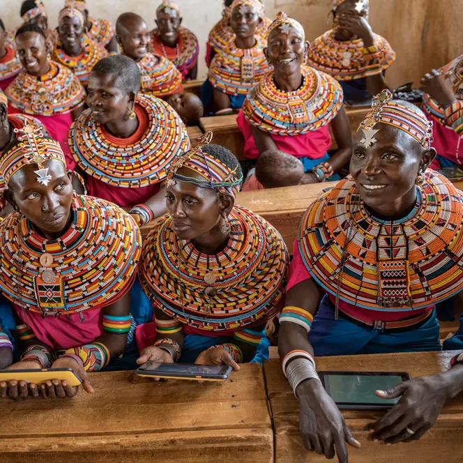 Women from the Samburu tribe in Kenya sitting on a wooden bench in traditional clothes and smiling.
