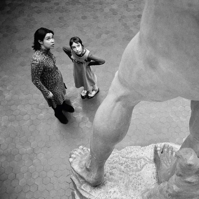 Two people stand in front of a large statue and look upwards.