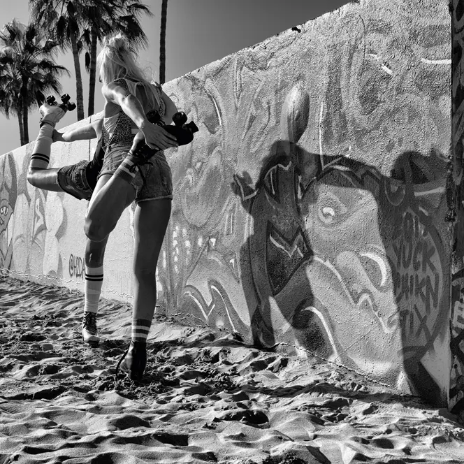 A boy looks behind a graffiti-painted wall at two women on roller skates warming up.