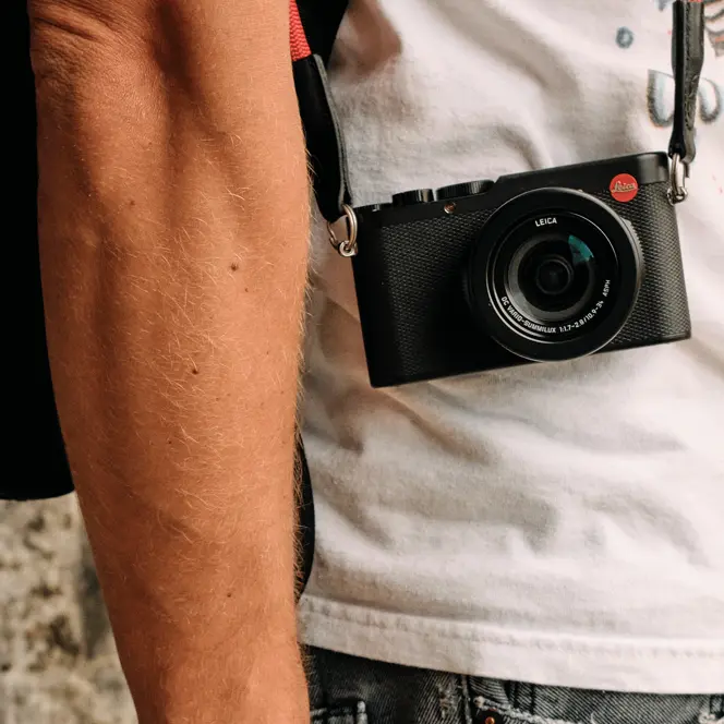 Side shot of a person with a Leica camera hanging in front of his body..