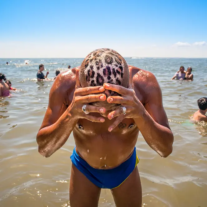 A man with a leopard print on his head is standing in the water. Several people are bathing in the sea around him.
