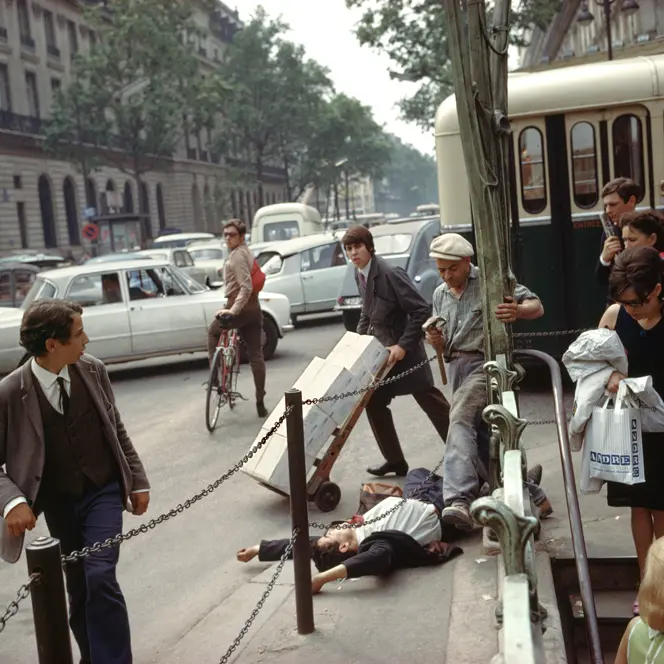 A young man in a suit and tie lies on his back with arms stretched above his head, directly next to the metro station