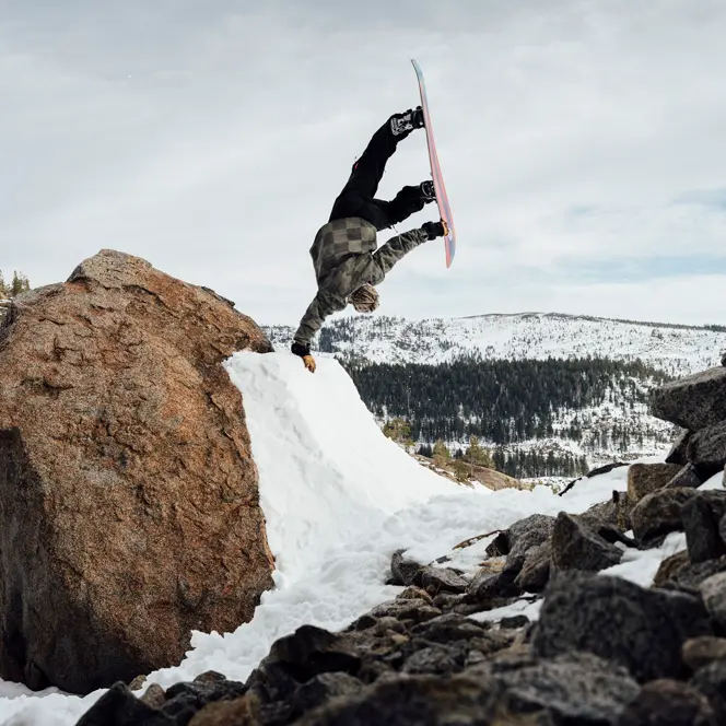 Snowboarder does a one-armed handstand on a ramp in the mountains