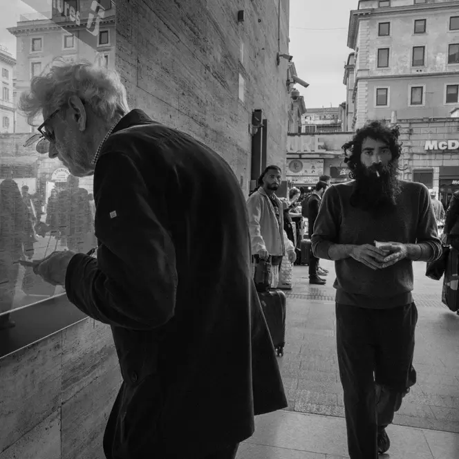 Elderly man in the city looking at a train timetable behind a pane of glass.