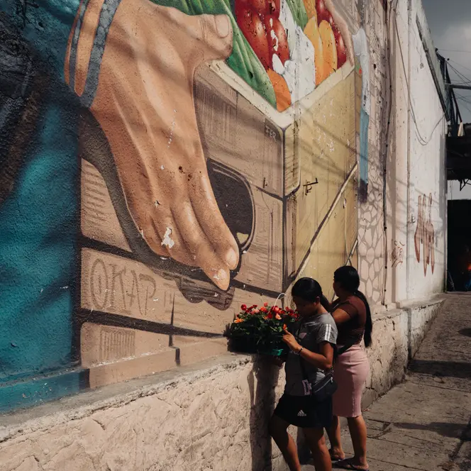 Two women with fruit baskets in front of a big fruit graffiti