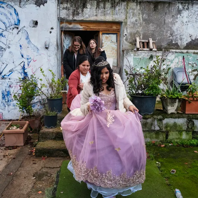 Young woman in a formal quinceañera dress surrounded by family, capturing a milestone celebration within a modest residential setting.