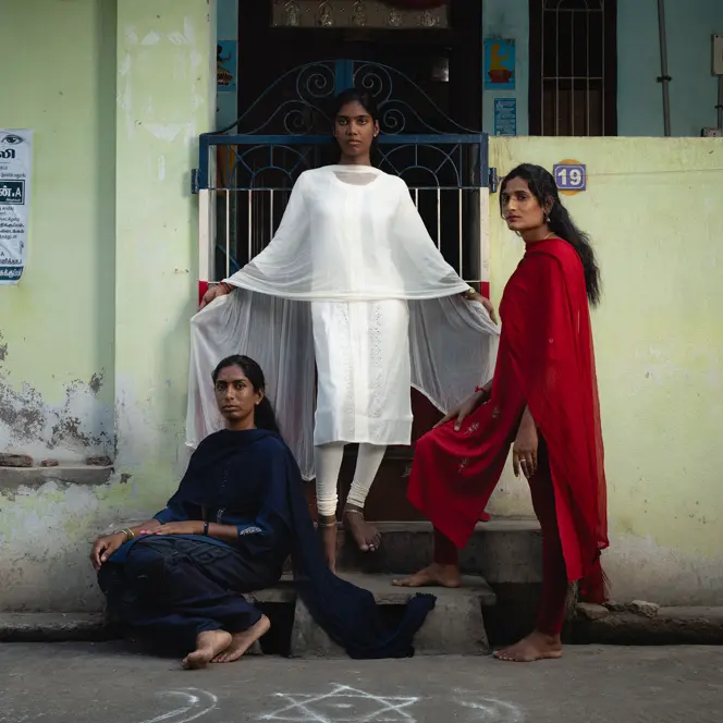 Trois femmes vêtues de bleu, de blanc et de rouge posent devant un bâtiment.