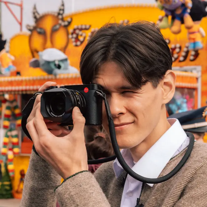 Teo Crawford using a Leica Q3 at Munich Oktoberfest, capturing candid moments in front of a colorful fairground booth during the world's largest folk festival.