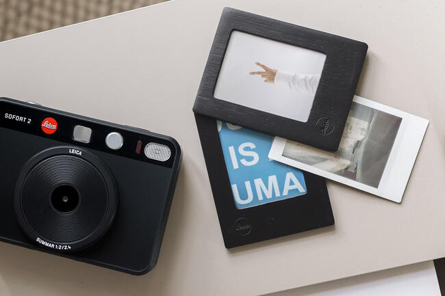 The prints in a frame next to the Leica Sofort 2 black.