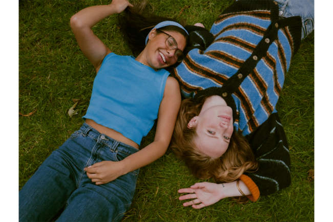 Portrait of two women laying in grass.