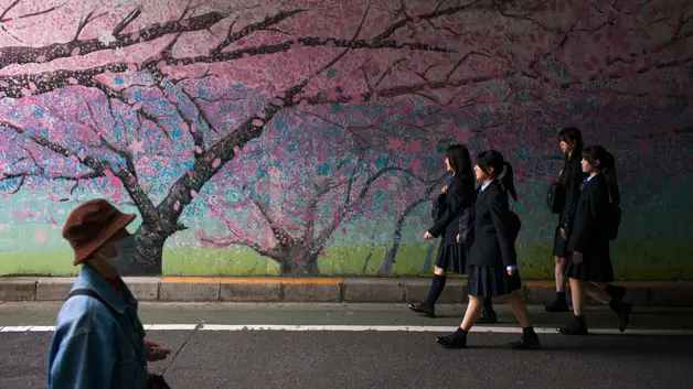 Schoolgirls in uniform walk past street art in Tokyo