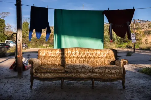 Vintage sofa placed outdoors beneath hanging laundry, creating an intimate scene of domestic life and urban living conditions.