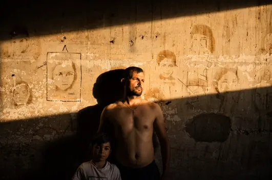 Man and child illuminated by dramatic sunlight against a weathered wall, capturing family bonds, resilience, and everyday life.