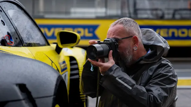 Photographer Callo Albanese capturing a race car in wet conditions with a Leica camera, highlighting motorsport photography in action.