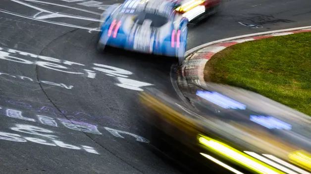 High-speed race cars navigate a circuit corner, captured with dynamic motion blur and vivid light trails.