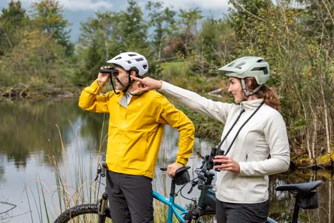 Two cyclists standing next to their bikes and looking through their Leica Noctivid Compact