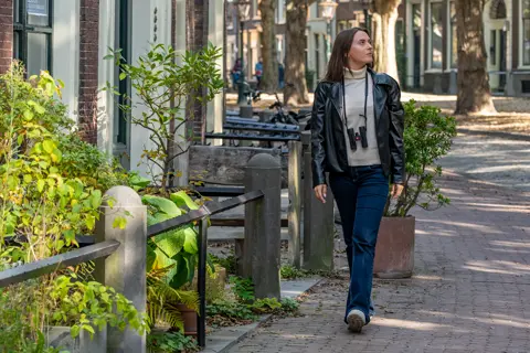 Woman is walking down the street with her Leica Noctivid Comapct