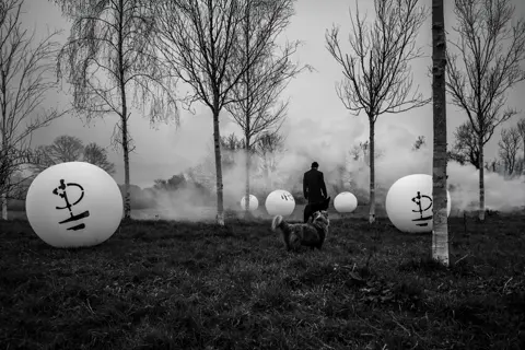 Black and White image of David Gilmour in a misty field with a dog.