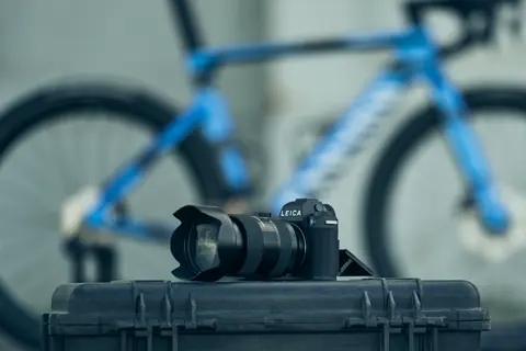 Leica SL3-P liegt auf Koffer und im Hintergrund steht blaues Rennrad