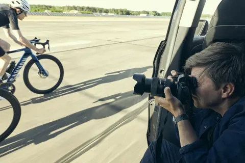 Tino Pohlmann fotografiert zwei Rennradfahrer aus dem fahrenden Auto auf Flugplatz