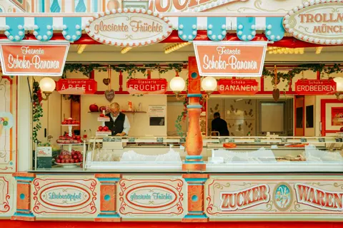 Traditional Oktoberfest candy stand selling chocolate-covered fruit, caramel apples, and sweets, showcasing the colorful food culture of Munich's folk festival.