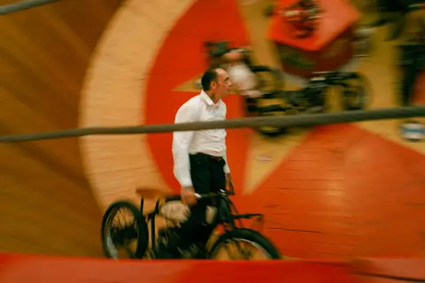 Motion-blur photograph of a cyclist riding inside the Oktoberfest Wall of Death attraction in Munich, capturing speed, skill, and fairground excitement.