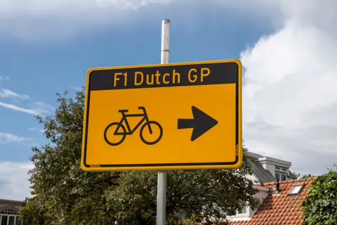 Yellow directional sign reading “F1 Dutch GP” with a bicycle symbol and arrow pointing toward the Dutch Grand Prix in Zandvoort.