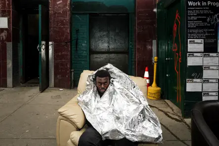 A man is sitting in an armchair by the roadside, wrapped in cling film 