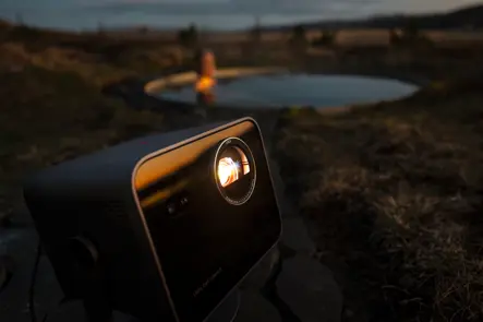 A woman is sitting by the pool in the evening, watching the projection from the Leica Cine Compact 1