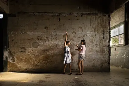 Two young girls playing inside a weathered building, capturing childhood, imagination, and everyday life in a communal setting.