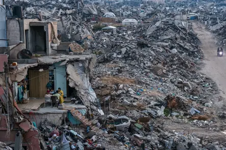 A family remains in the ruins of their partially destroyed home amid widespread devastation in Gaza. Documentary photography capturing conflict, displacement, urban destruction, and civilian life after war.