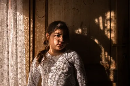 Young girl illuminated by window light indoors, capturing an intimate portrait with natural light and shadow.