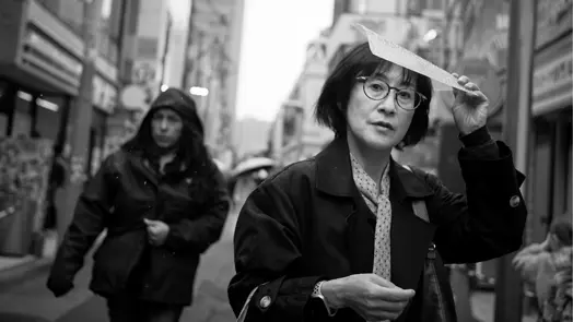 Woman shielding herself from the rain on a busy Tokyo street, captured in black-and-white street photography.