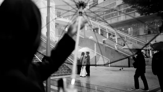 Transparent umbrellas frame pedestrians in a rainy Tokyo cityscape with layered urban reflections.
