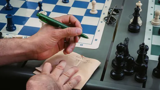 Hand recording the score beside an outdoor chess game.