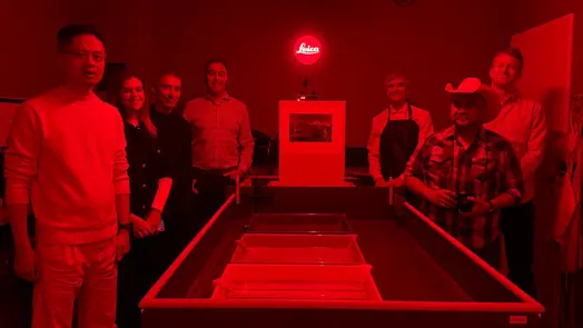 Group gathered around a photographic print in a red-lit darkroom.