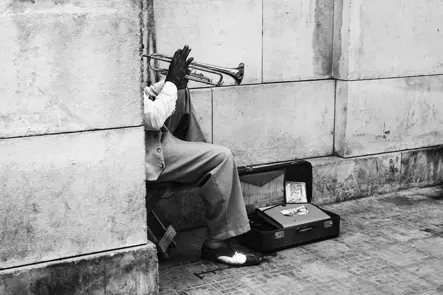 Black-and-white street photograph of a trumpet player performing beside an open case in Cuba, capturing music and everyday urban life.