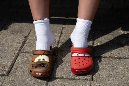 Close-up of a person wearing mismatched Cars-themed clogs featuring Lightning McQueen and Mater, paired with white socks.
