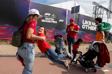 A smiling child in Ferrari red swings playfully from an adult’s arms outside the Formula 1 Dutch Grand Prix venue in Zandvoort.
