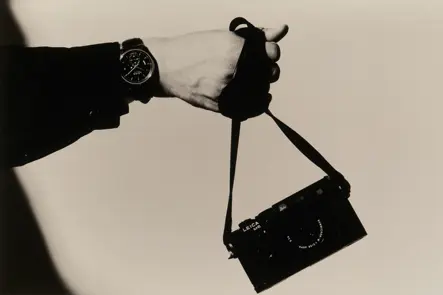 Close-up of a hand wearing a Leica wristwatch while holding the strap of a Leica M6 camera in a minimalist black-and-white composition.